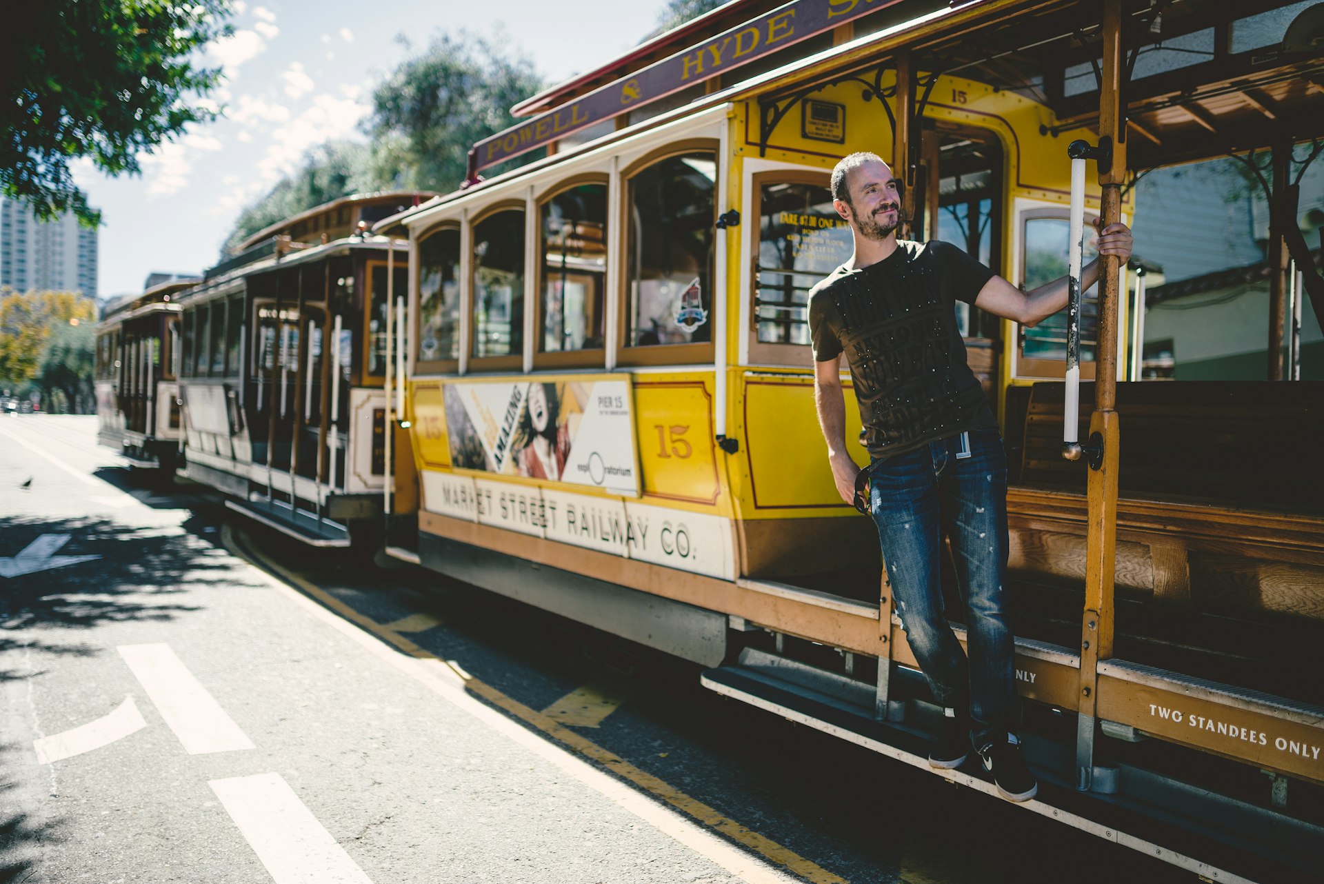 A man leans out of an open-sided cable car in San Francisco